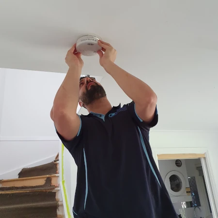 Electrician installing Quell battery photoelectric smoke alarm in a residential building